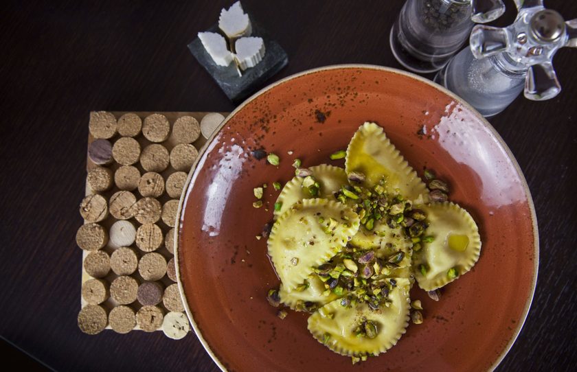 Ravioli with crushed pistachio on a terracotta plate, on a cork mat, from above