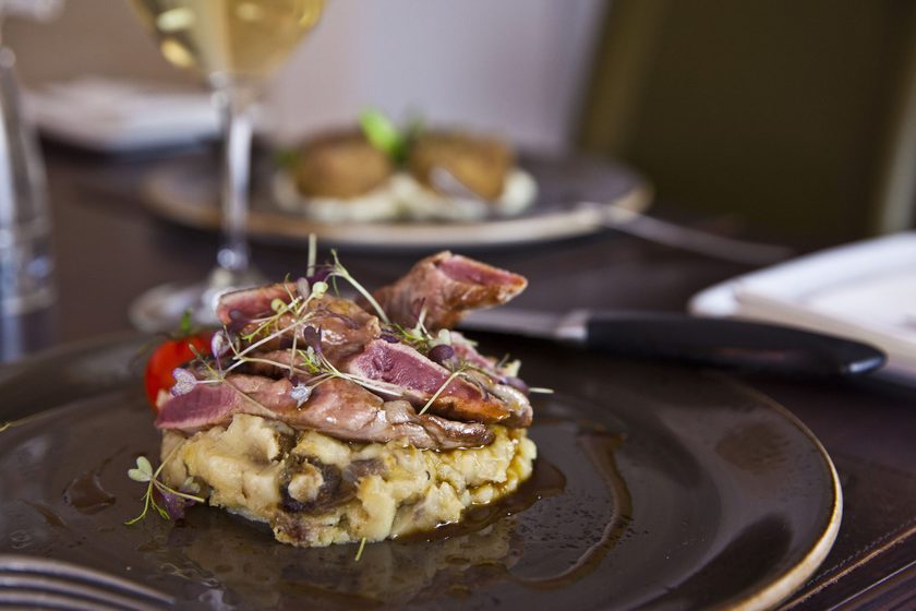 Sliced lamb on crushed potato with jus, a cherry tomato and micro herbs