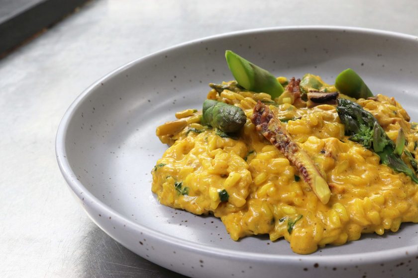 Saffron risotto with octopus and asparagus in a grey speckled bowl