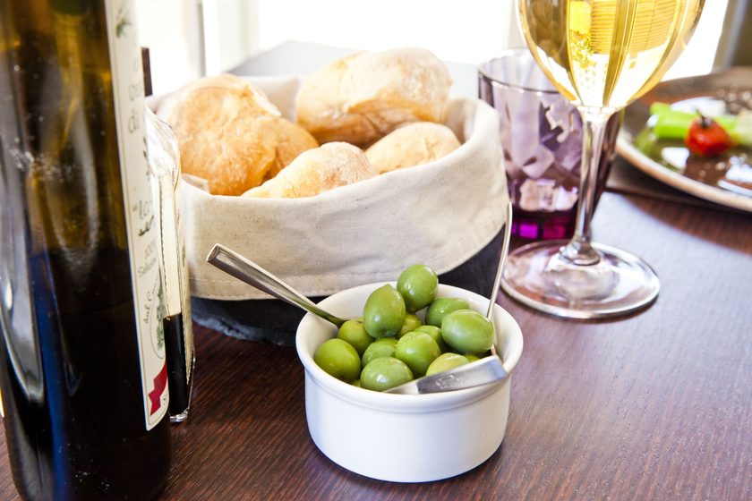 Bread rolls in a cloth basket, green olives and a bottle of olive oil on the table