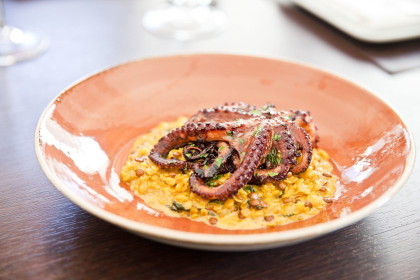 Grilled octopus tentacle on saffron risotto in a terracotta bowl