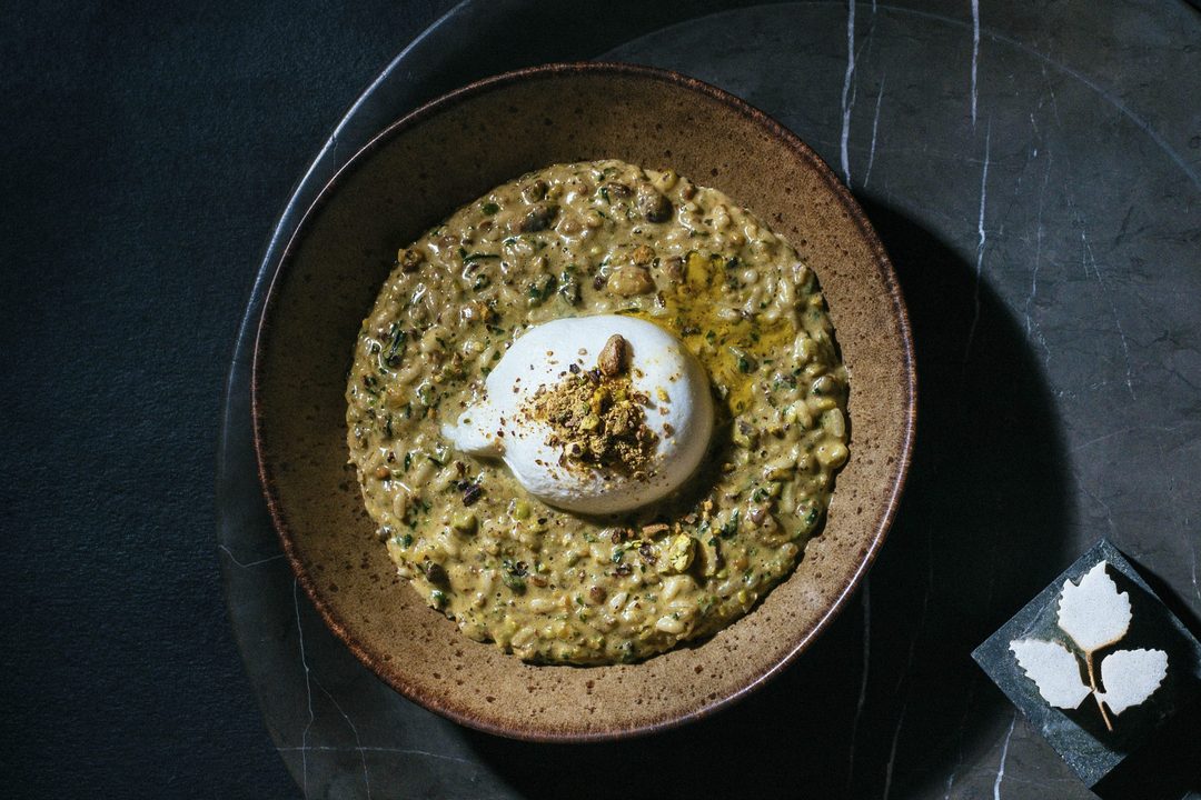 Pistachio risotto with burrata in a brown stoneware bowl on dark marble