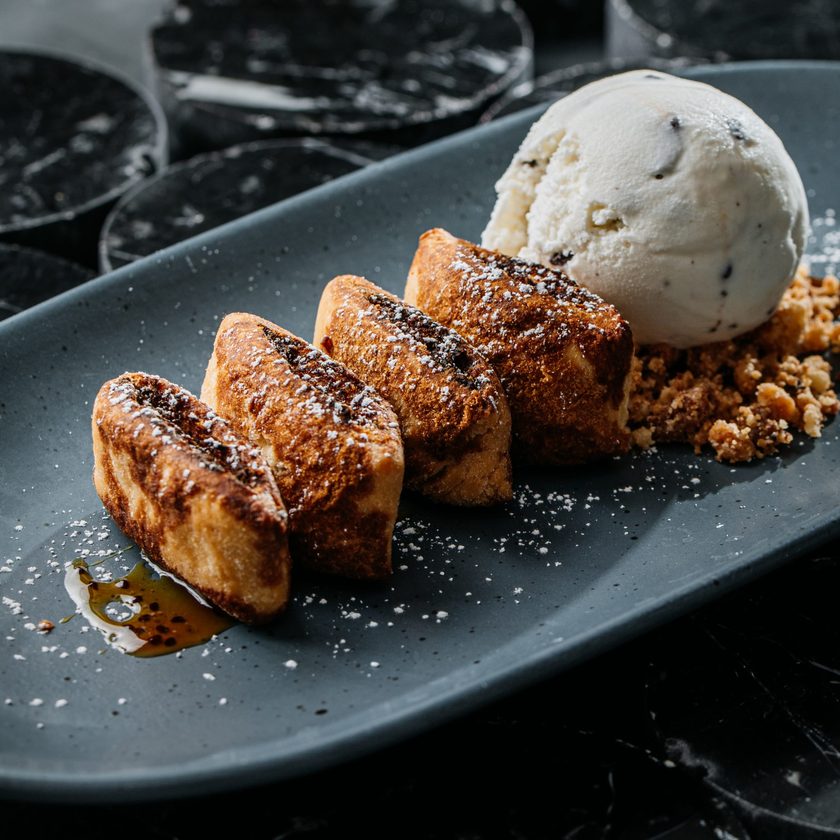Imqaret date fritters in a row with ice cream and crumble on a dark slate plate