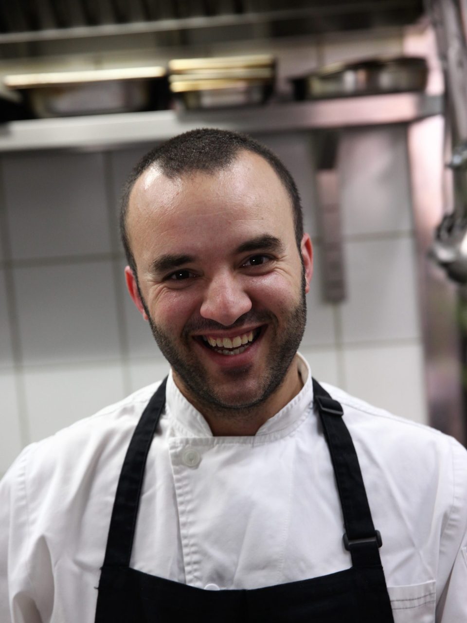 Chef patron Matthew Schembri in whites and a black apron, smiling in the kitchen